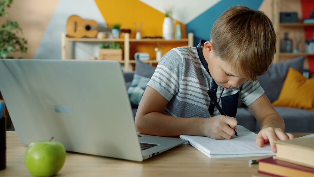 ノートに書きながらオンライン授業を受ける子どもと見守る保護者
